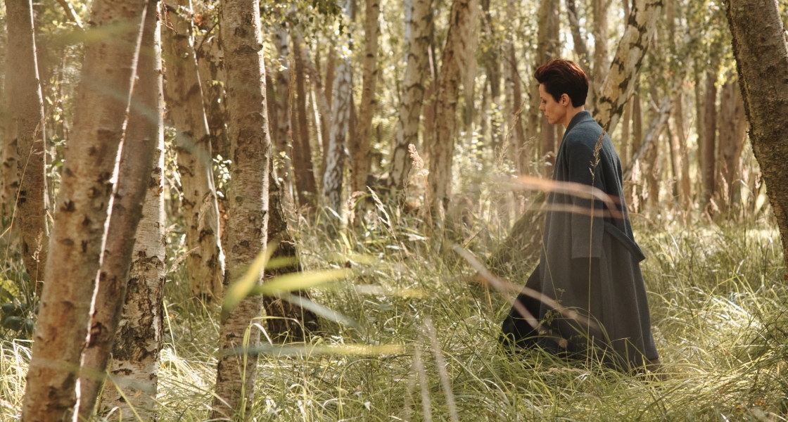 Woman in a cloak walking through the woods 